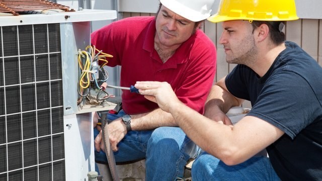 Two technicians servicing the wiring of an outdoor air conditioning unit