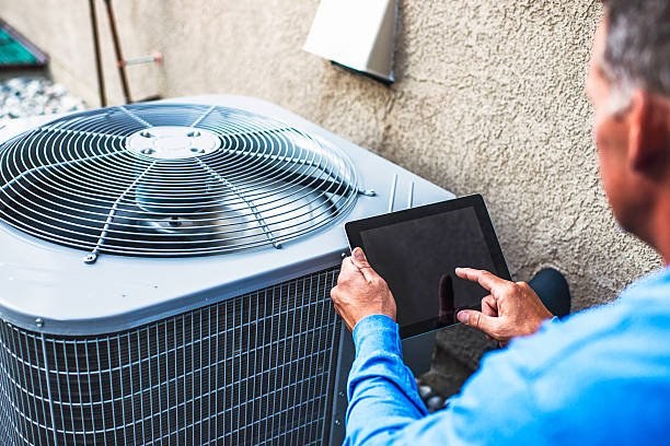 Technician checking an outdoor condenser with a tablet during a diagnosis