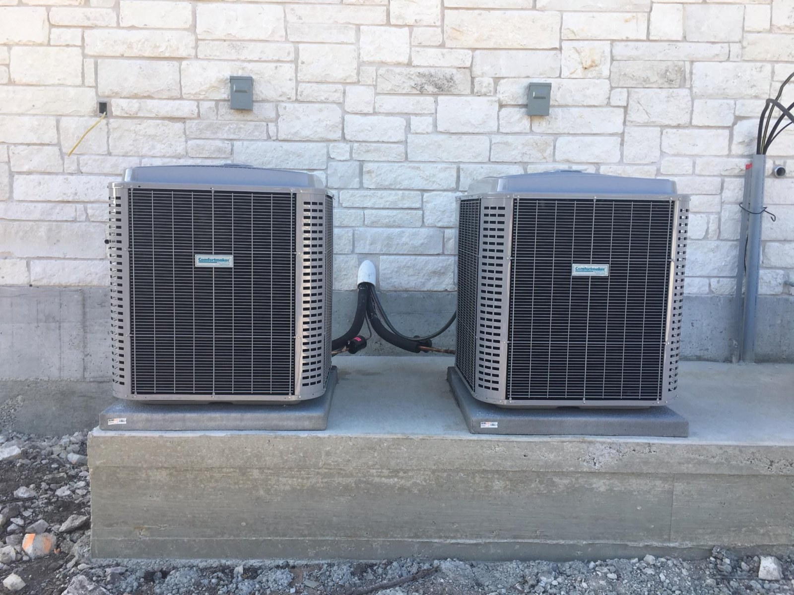 Two new outdoor condenser units installed beside a stone home